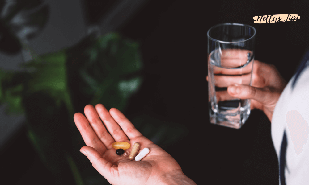 Hand som håller olika vitaminer och ett glas vatten.