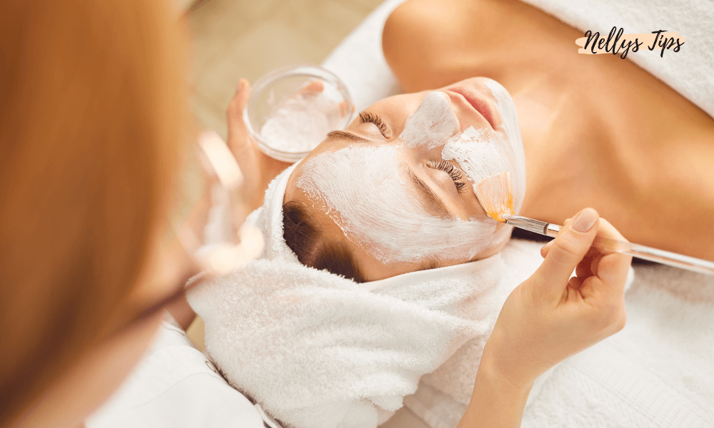 Kvinna får ansiktsbehandling med peelingmask applicerad med pensel på ett spa, avslappnande hudvårdsrutin.