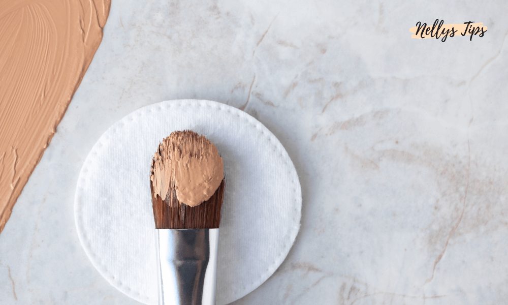 Makeupborste med beige CC-cream placerad på en bomullsrondell, utsmetad kräm syns i hörnet.