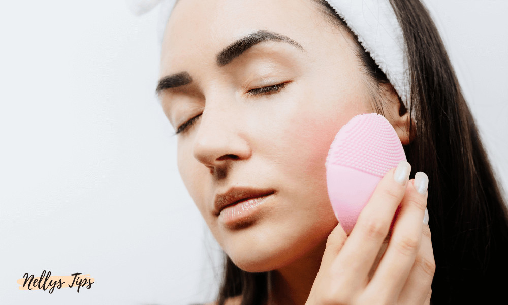 Kvinna använder en rosa elektrisk ansiktsborste för skonsam rengöring och massage av ansiktet.