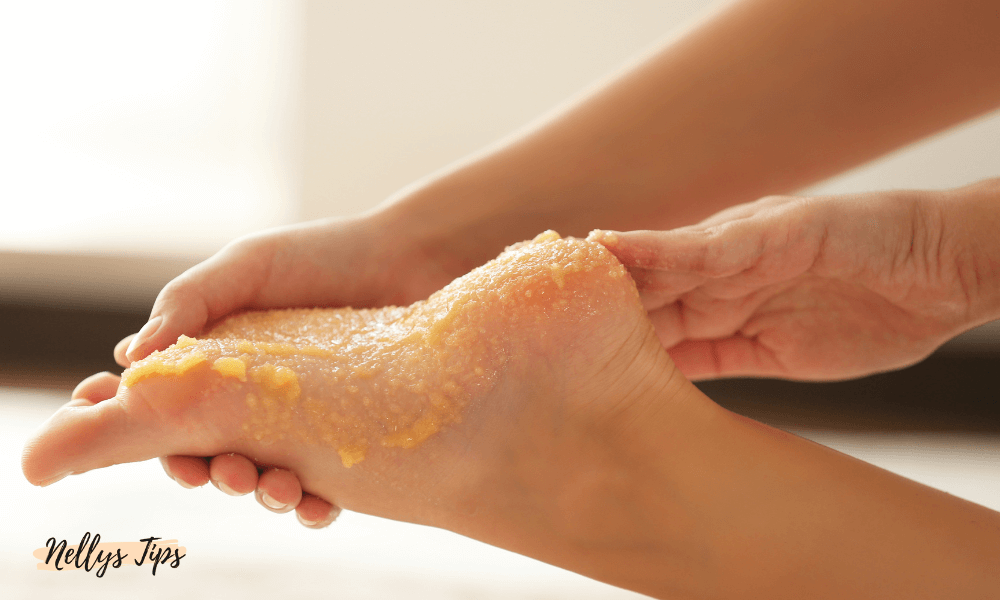 Hand applicerar sockerskrubb på fotsula för exfoliering och silkeslena fötter.