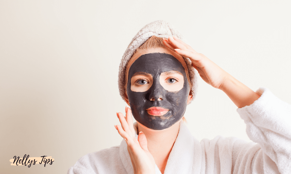 Kvinna med svart kolmask och vit morgonrock – applicerar djuprengörande mask för klarare hud och minskade porer.
