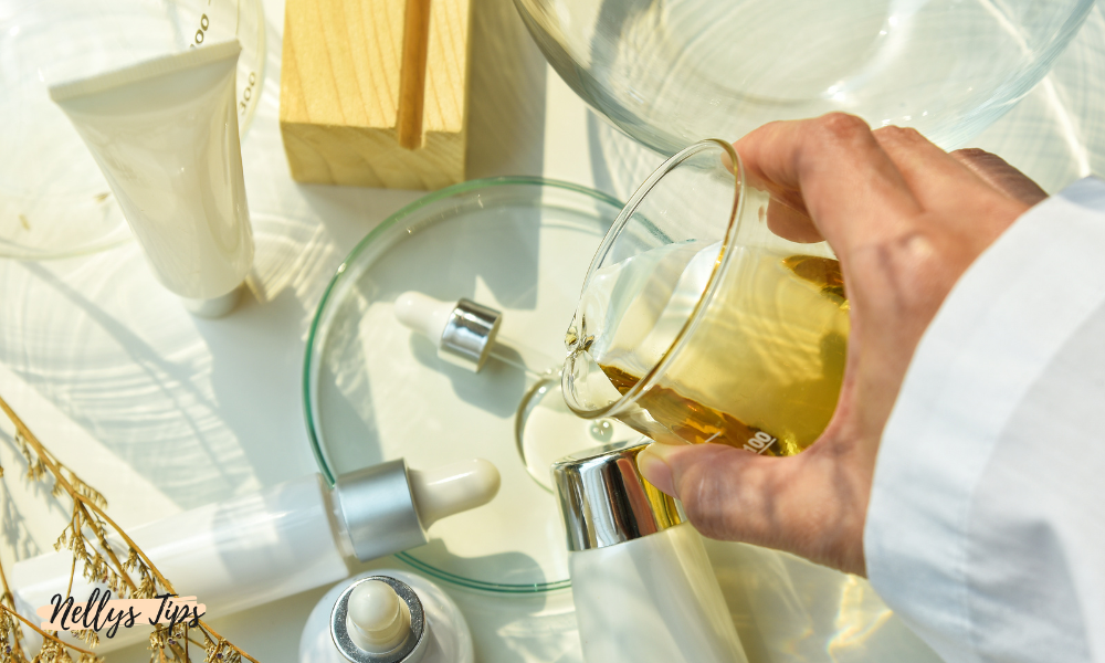 Hand häller olja i glasbägare bland naturliga hudvårdsprodukter med pipetter och tuber