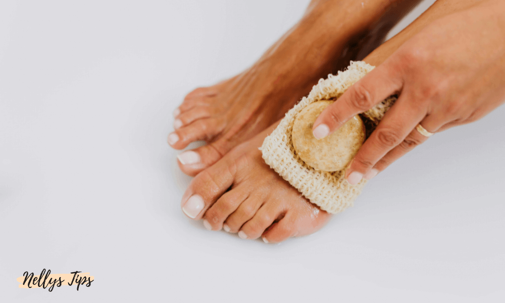 Person exfolierar fötterna med skrubbhandske och tvål för mjuk och ren hud.
