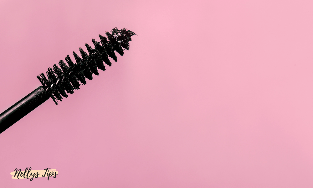 Öppen rosa mascara med svart borste ligger på matchande rosa underlag.