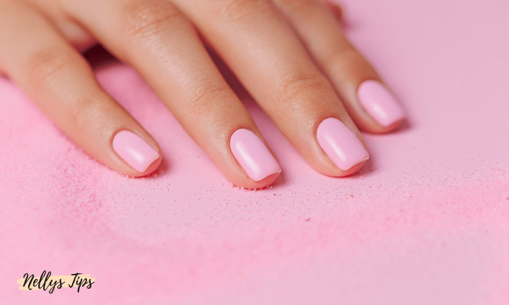 Närbild på hand med rosa nagellack på välvårdade naglar mot puderrosa underlag.
