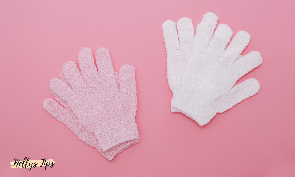 Två par skrubbhandskar i rosa och vitt liggandes på rosa underlag för exfolierande hudvård.