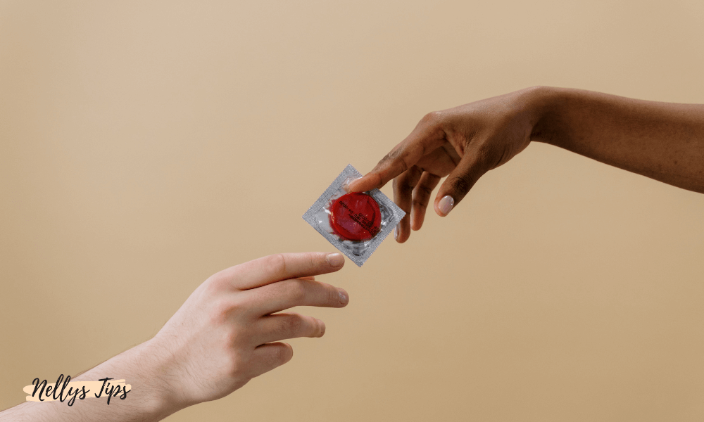 Två händer som räcker över en förpackad röd kondom till varandra.