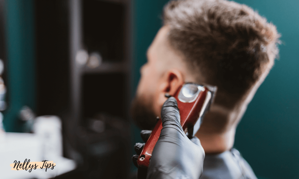 Frisör trimmar hår med röd trimmer nära örat, fokus på precision och konturklippning.