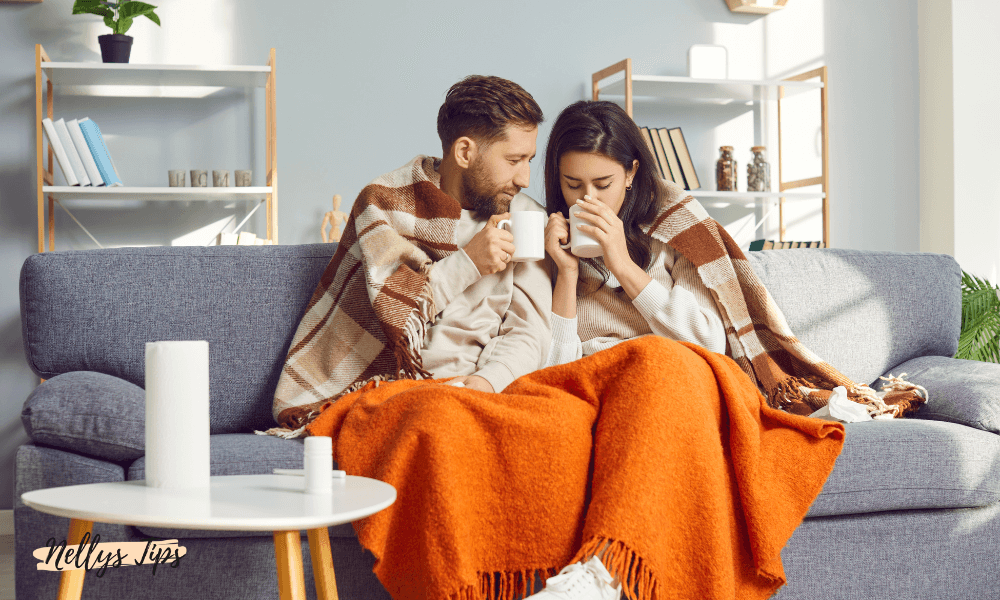 Par under filt på soffa dricker varma drycker och njuter av värmen tillsammans