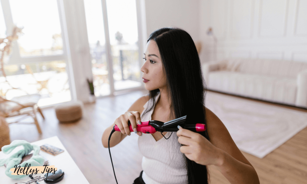Kvinna stylar långt mörkt hår med rosa och svart plattång – ger ett rakt och glansigt resultat.