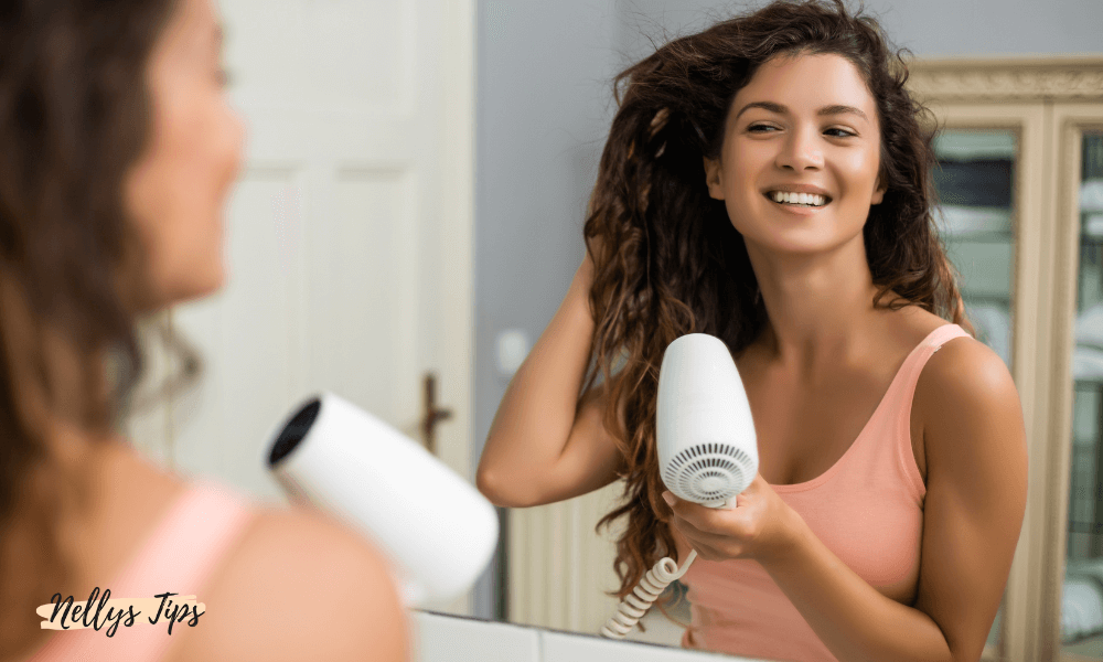 Kvinna fönar håret med vit resehårfön framför spegel – enkel och smidig vardagsstyling.