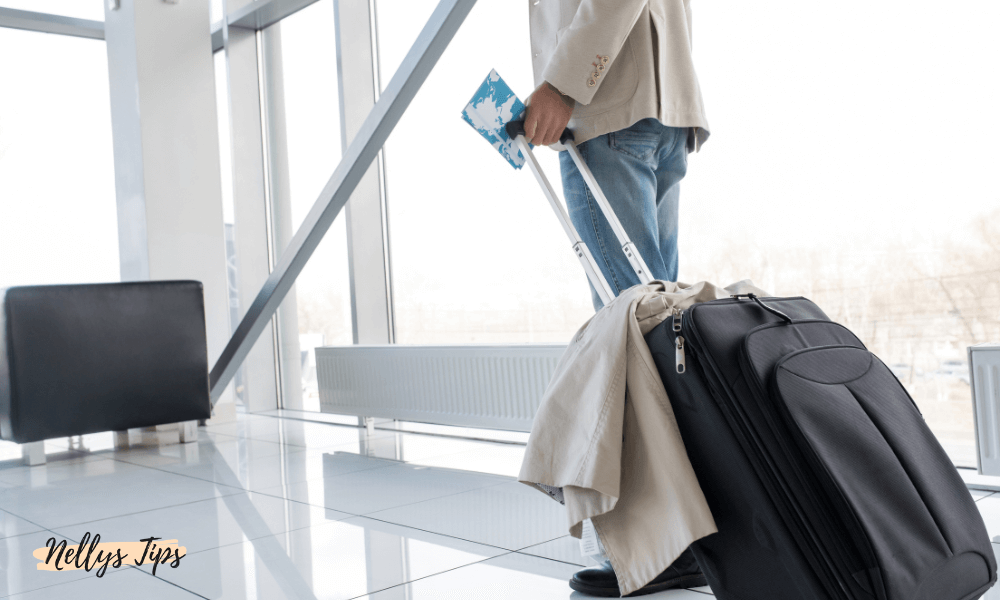 Person med kabinväska på flygplats, håller boardingkort och jacka över väskhandtaget.