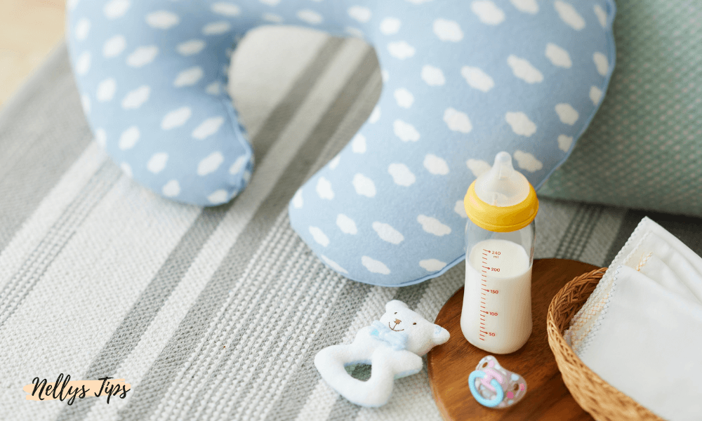 Amningskudde i blått med molnmönster, nappflaska och babyartiklar på en filt