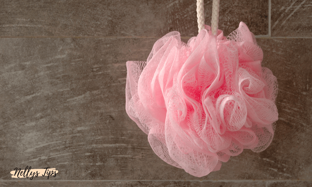 Rosa badpuff hängande i duschutrymme, används för löddrande kroppsrengöring.