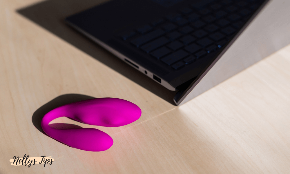 Fjärrstyrd rosa vibrator placerad på ett bord bredvid en bärbar dator