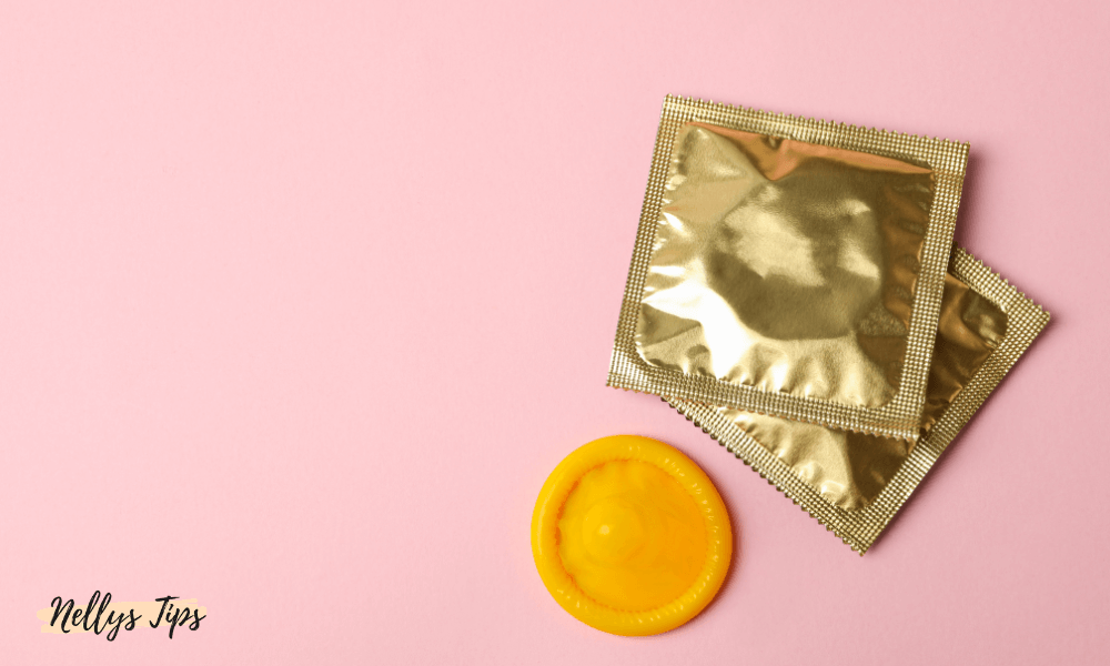Två oöppnade gyllene kondomförpackningar och en gul kondom på rosa bakgrund.