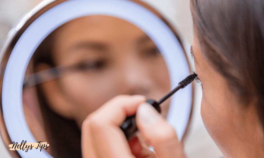 Kvinna applicerar mascara framför rund LED-spegel för optimal belysning.
