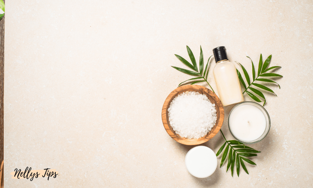 Flatlay med kroppsvårdsprodukter som duschkräm, salt, ljus och gröna blad i spa-inspirerad miljö.