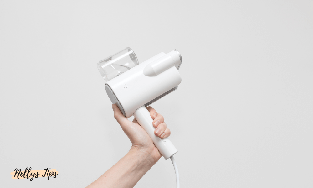 Hand håller i modern vit steamer med genomskinlig vattentank och stilren design för effektiv strykning.