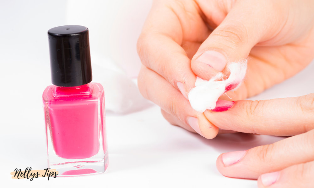 Hand som tar bort rosa nagellack med bomull, bredvid en flaska nagellack.