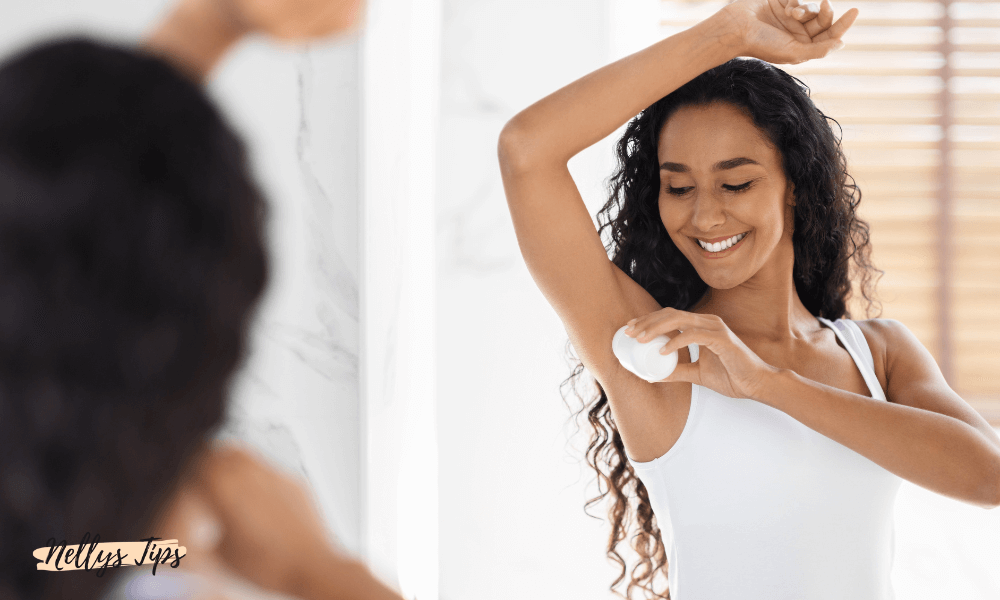 Leende kvinna applicerar deodorant framför spegeln med vit roll-on, visar vardaglig hygienrutin.