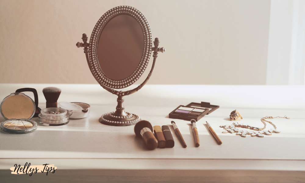 Vintageinspirerad sminkspegel på sminkbord med borstar, puder och smycken.