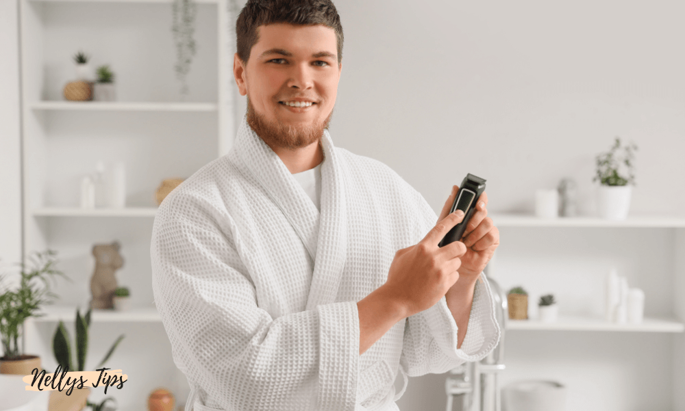 Man i vit morgonrock visar en kroppstrimmer för hårborttagning och grooming av kroppen.