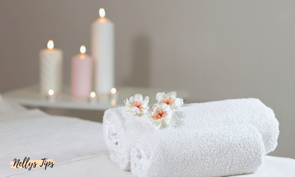 Vita rullade handdukar med blommor i ett avslappnande spamiljö med tända ljus.