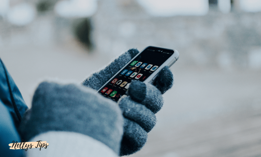 Person med gråa touchhandskar använder smartphone utomhus i kallt väder.