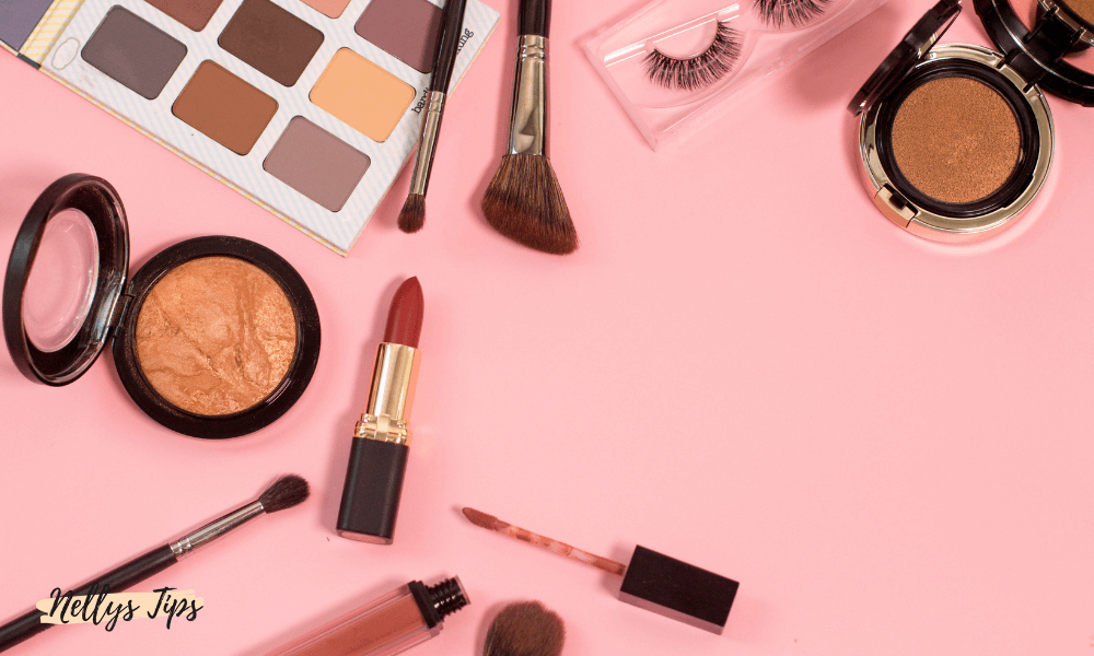 Makeup-produkter som ögonskuggor, borstar och läppstift på rosa bakgrund i sminkorganisering.